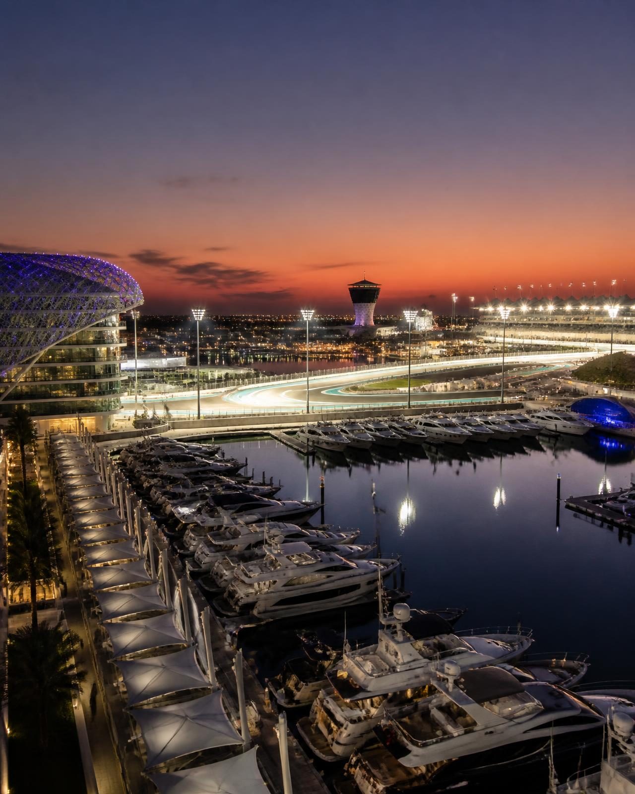 Yas Marina at dusk with yachts moored beside a floodlit circuit