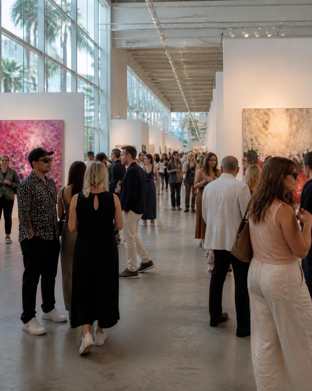 Visitors among white booths and large canvases at a Miami art fair