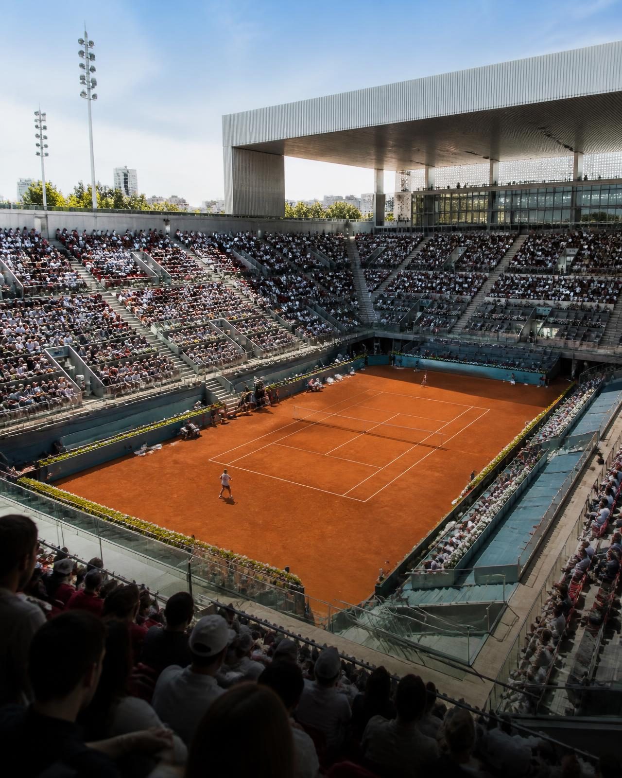 A clay court inside a modern Madrid tennis arena in spring sunshine