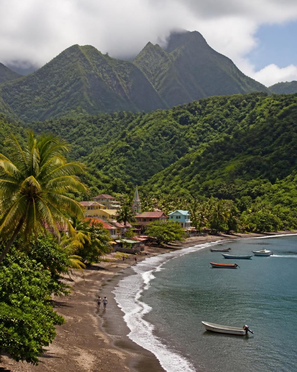 Green volcanic peaks above a French Caribbean fishing village and dark sand bay