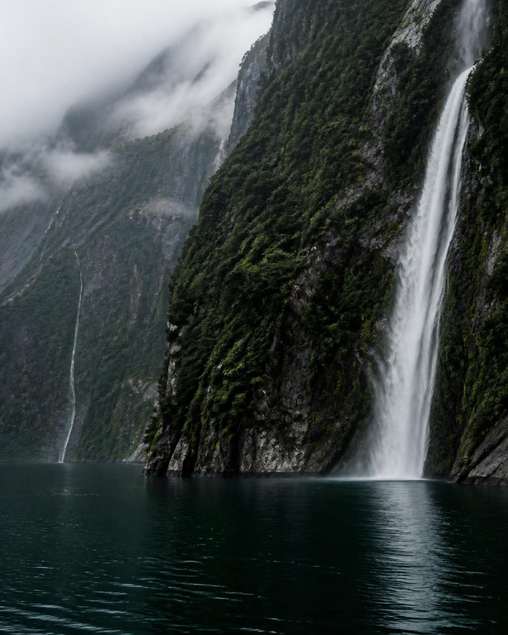 Waterfall dropping down forested cliffs into a deep fiord in New Zealand