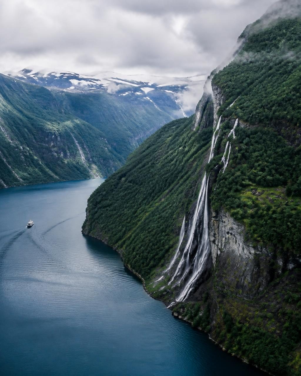 Green cliffs and waterfalls dropping into a deep Norwegian fjord