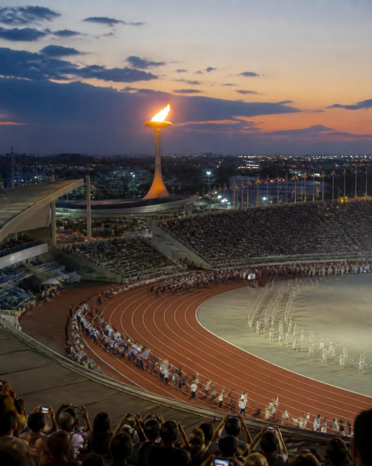 An athletics stadium at dusk during an opening ceremony, cauldron lit