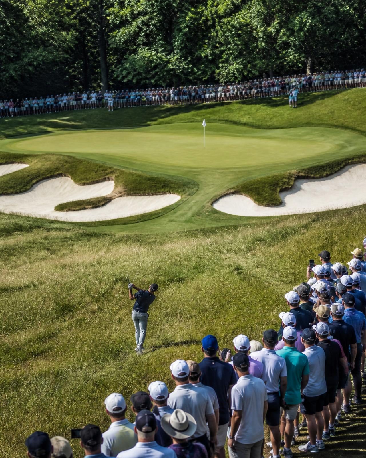 A championship golf green with deep bunkers and spectators lining the fairway